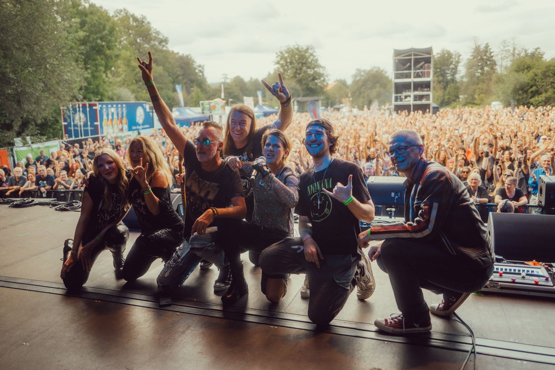 Group of musicians on stage posing with a cheering festival crowd in the background.